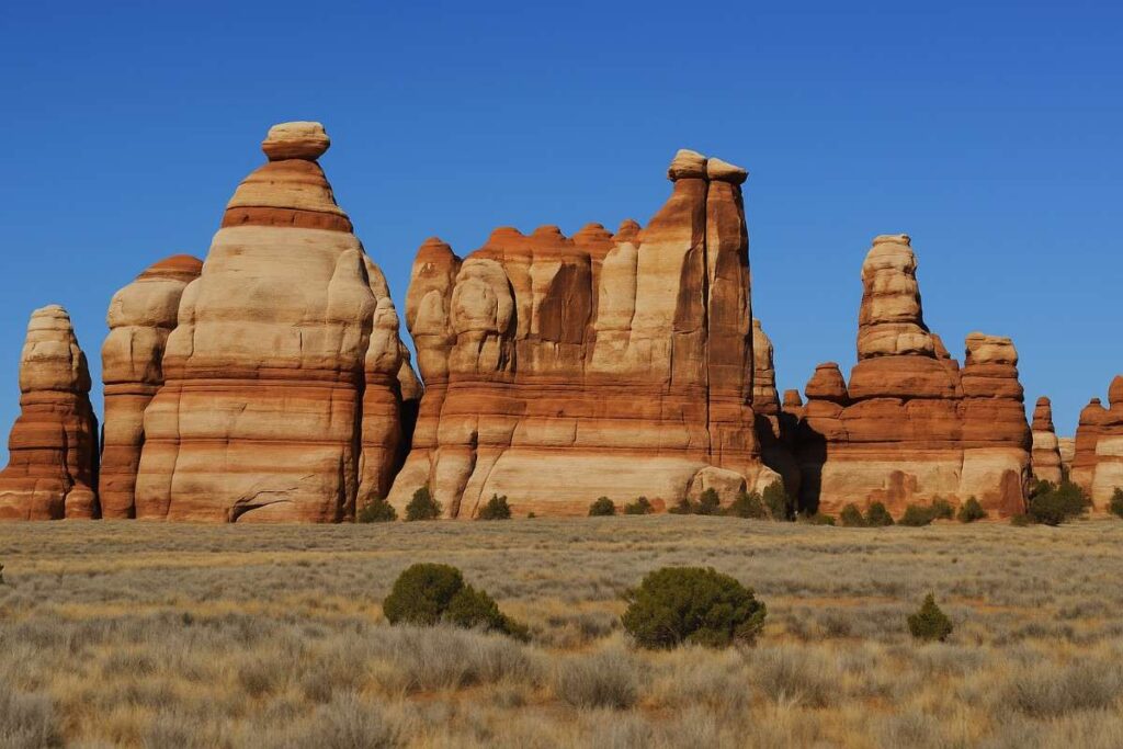 A scenic view along the Maze Loop $ Chesler park Trail in Canyonlands National Park, showcasing rugged red rock formations, desert vegetation, and the vast natural beauty of the American Southwest under a clear blue sky.