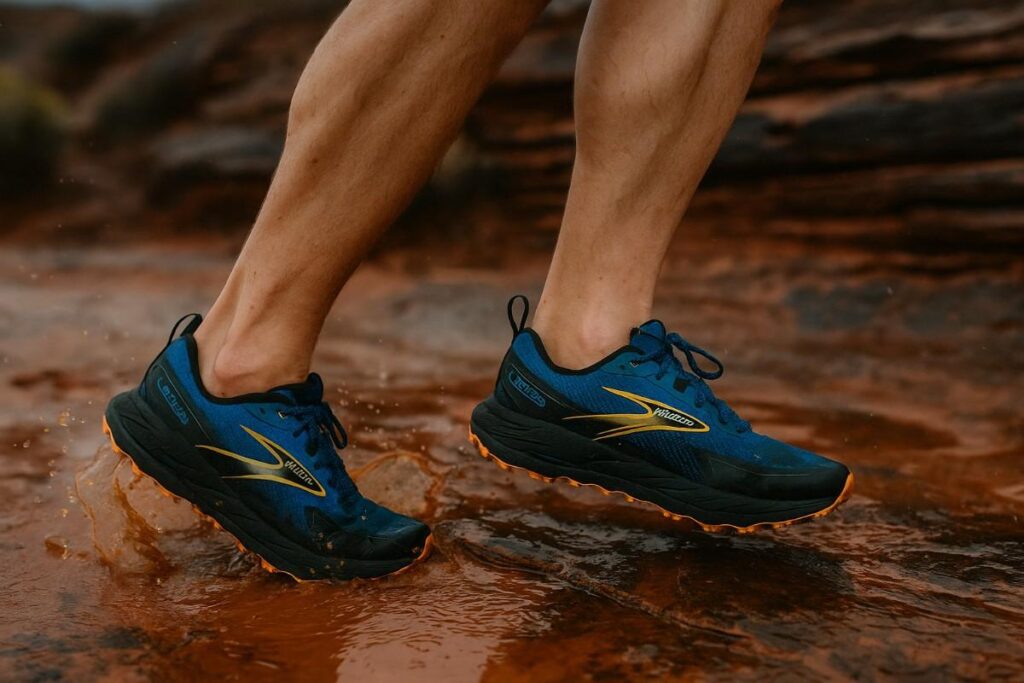 Close‑up of Brooks Cascadia 18 shoe splashing through muddy puddle on slick sandstone.