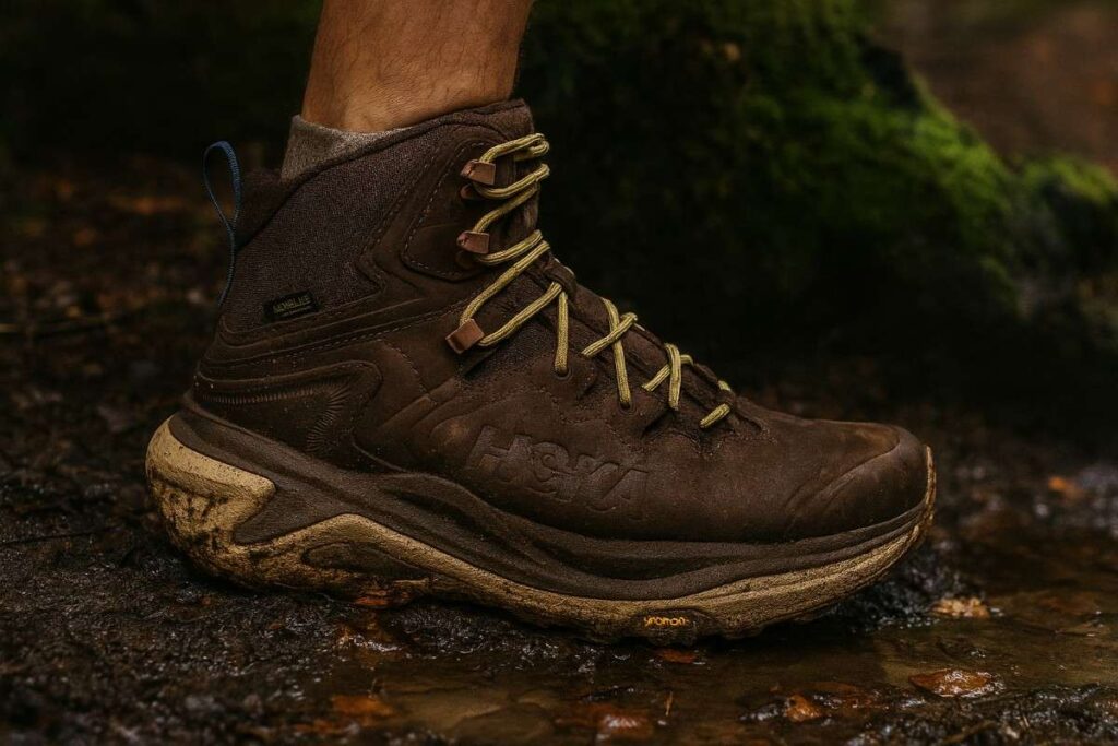 Hiker legs wearing Hoka Kaha 3 GTX stepping through muddy forest trail — shock-absorbing trail boots.