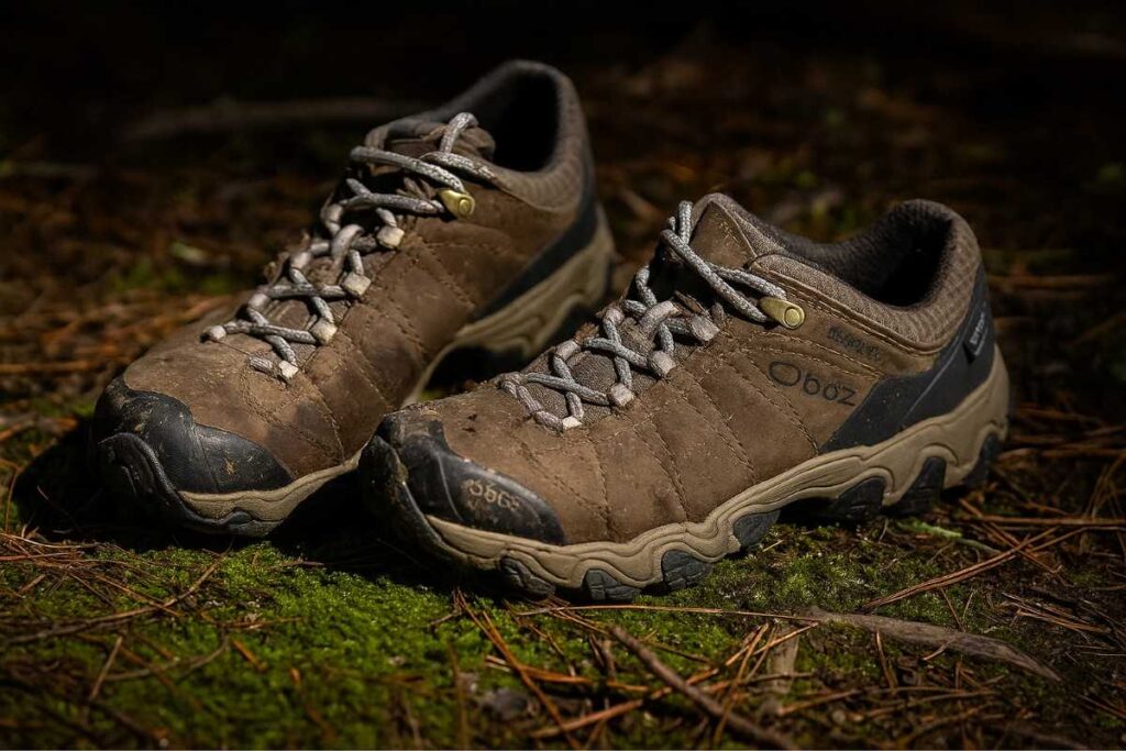 Oboz Bridger Low B-DRY hiking shoes on a damp forest trail with pine needles and moss.