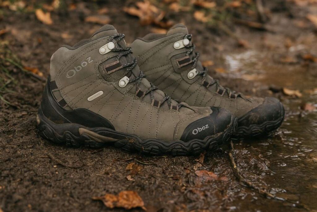 Close-up of Oboz Bridger Mid B-DRY hiking boots on muddy forest trail with wet soil.