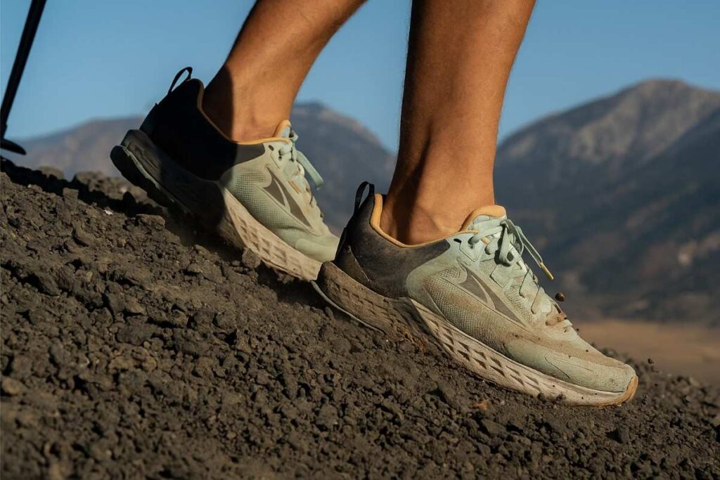 Hiker wearing Altra Timp 5 shoes descending volcanic scree slope in high desert.