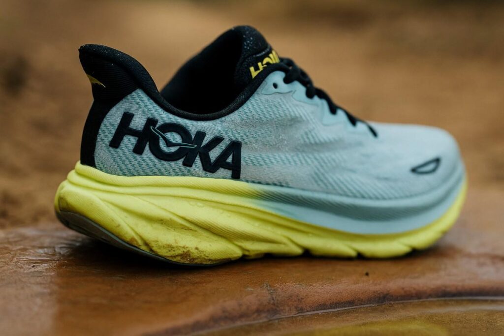 Close up of Hoka Clifton 9 displayed on wet rocky surface.