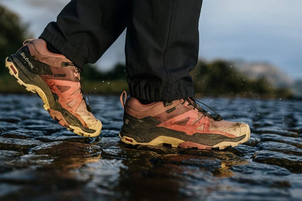 Female hiker wearing Salomon X Ultra 4 GTX shoes crossing wet cobblestone trail after rain.