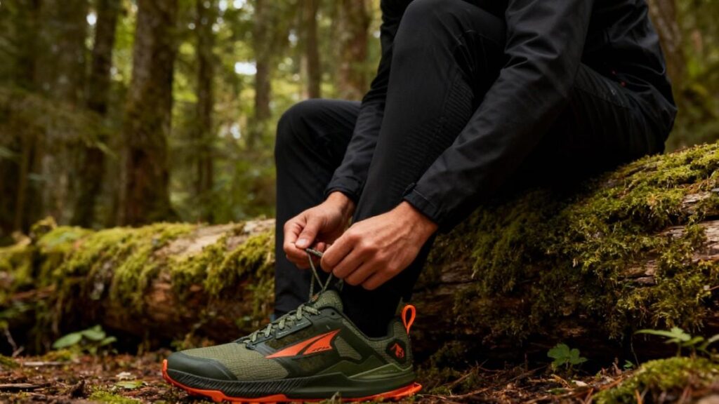 Hiker sitting on a wooden log lacing up his Altra Lone Peak 8.
