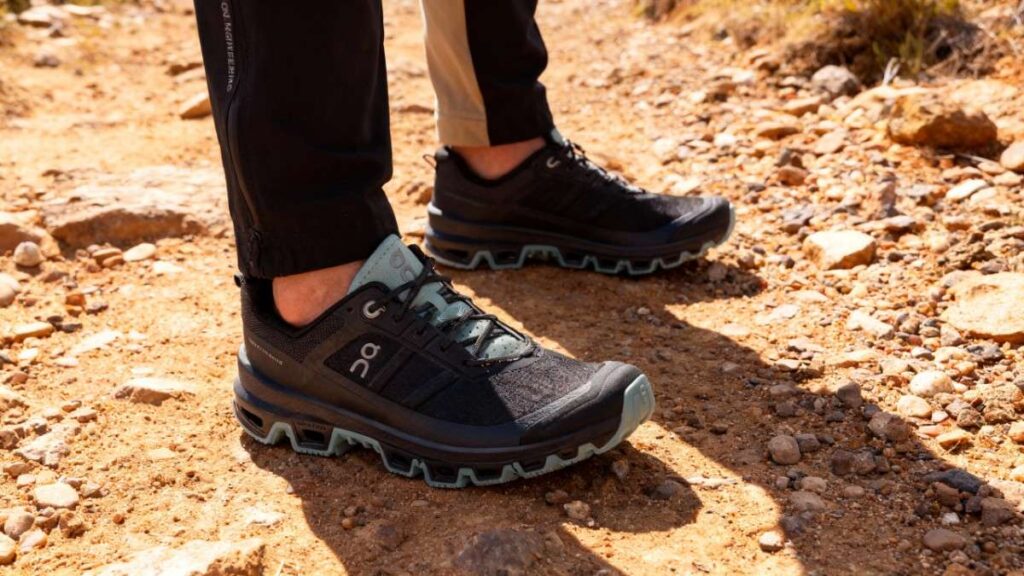 Hiker's legs shot wearing On Cloudventure and standing on rocky terrain.