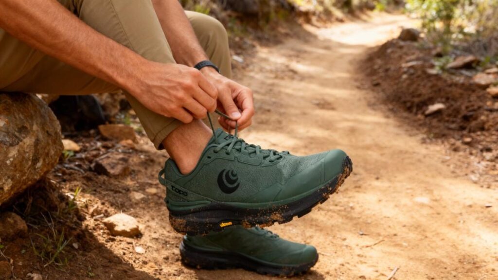 Hiker sitting on a rock lacing his Topo Athletic Traverse.