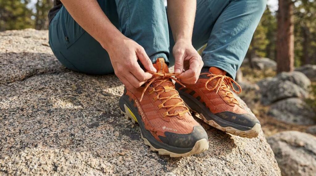 Hiker lacing up his Merrell Moab Speed 2 GTX while sitting on a boulder. 